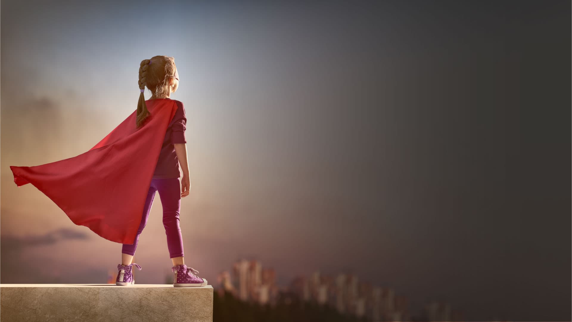 child in a red cape looking out over the city